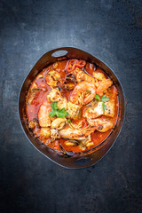 Traditional Spanish sarsuela fish stew with prawns, mussels and fish as top view in a modern design Japanese cast-iron roasting dish