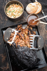 Traditional barbecue pulled pork piece of Bosten butt torn to bits with coleslaw and burger as top view on a board