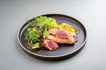 Gebratene Schweine Ferkel Filet mit Bratkartoffel und Salat angeboten als closeup in einem Modern Design Teller mit  würziger Sauce