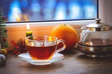 festive tea party. a cup of tea and a teapot. on the background of New Year and Christmas decorations. near the window with a blue, cold, winter background.