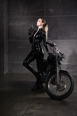 Obraz na płótnie Canvas Biker girl in a latex suit with gun in hand