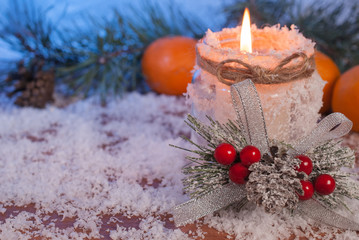 Burning candle, tangerines and fir branches on a wooden background. Cold toning