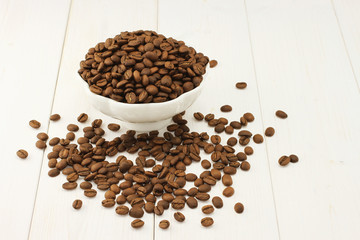 Fototapeta na wymiar Roasted coffee beans in bowl on white wooden background