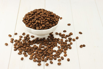 Roasted coffee beans in bowl on white wooden background