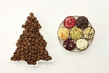 Roasted coffee beans in dish-spruce, set of chocolates in saucer on white wooden background