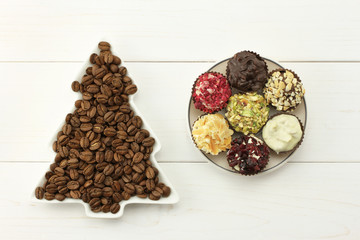 Roasted coffee beans in dish-spruce, set of chocolates in saucer on white wooden background