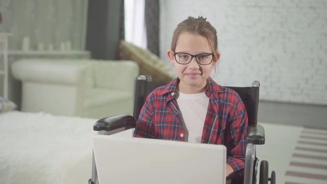 teenage disabled girl in a wheelchair using a laptop and looking at the camera smiling