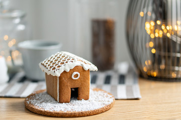 Gingerbread house on wooden table. Defocused garland lights on background. Christmas tree and Holiday mood. Morning in the bright living room.