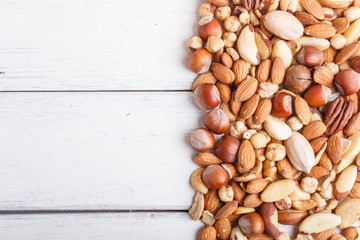 Mixed different kinds of nuts on white wooden background with copy space.
