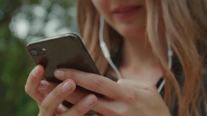 Extreme close-up of a beautiful caucasian woman using her phone out in nature with headphones in and smiling happily - Powered by Adobe