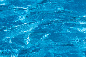 Blue and bright ripple water surface in swimming pool with sun reflection.