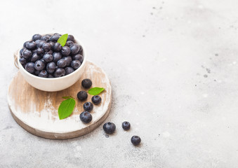 Fresh raw organic blueberries with leaf in white china bowl on stone kitchen background. Space for text