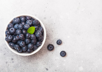 Fresh raw organic blueberries with leaf in white china bowl on stone kitchen background.