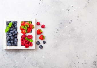 Fresh raw organic berries in white vintage wooden box on kitchen table background. Space for text. Top view. Strawberry, Raspberry, Blueberry and Mint leaf