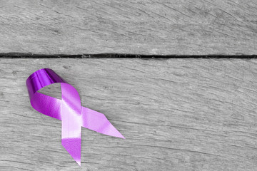 Purple ribbon for the awareness about the unacceptability of the violence against women on a dark gray rustic wooden surface