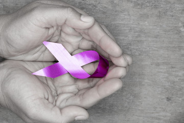 Woman's hands holding purple domestic violence awareness ribbon on table, healthcare and social problems concept.