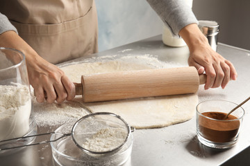 Woman rolling dough for cinnamon rolls on table, closeup