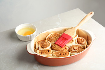 Baking dish with raw cinnamon rolls and pastry brush on table