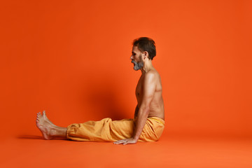 Old man practicing yoga doing stretching exercises against orange background