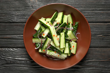 Plate with delicious cucumber salad on wooden background, top view