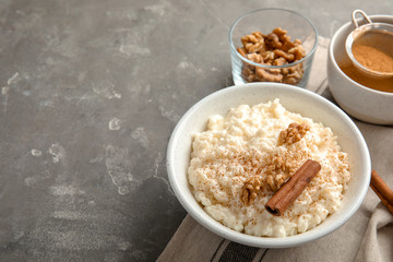 Creamy rice pudding with cinnamon and walnuts in bowl served on grey table. Space for text
