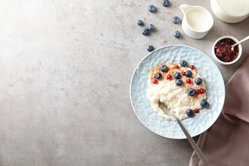 Creamy rice pudding with red currant and blueberries in bowl served on grey table, top view. Space for text