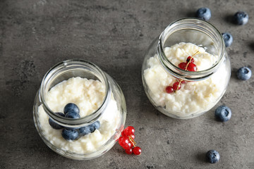 Creamy rice pudding with red currant and blueberries in jars on grey background