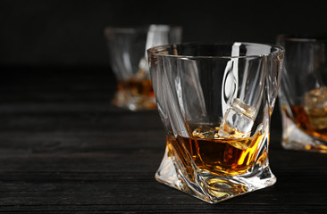 Golden whiskey in glass with ice cubes on wooden table. Space for text