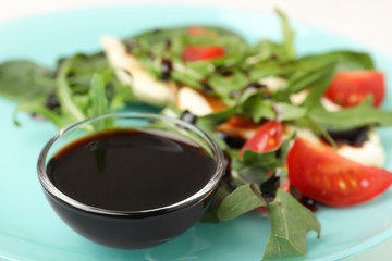 Bowl of balsamic vinegar on plate with vegetable salad, closeup