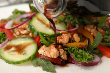 Pouring balsamic vinegar onto vegetable salad, closeup