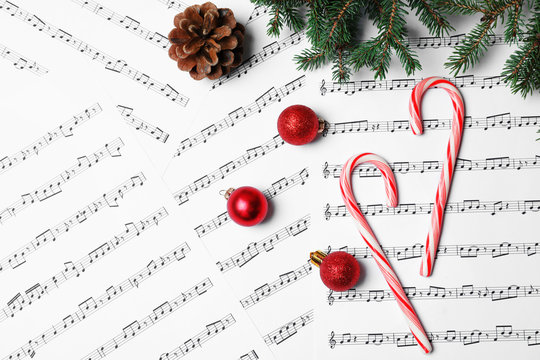 Composition with candy canes and Christmas balls on music sheets, top view