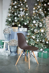 the brown chair on wooden legs costs in studio against the background of the decorated green Christmas tree and composition from cones in a vase