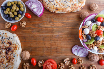 Frame made from tomatoes, mozzarella cheese, olives, kiwi, and walnuts on brown wooden background.
