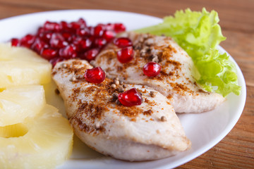 Fried chicken fillets with lettuce, pineapple and pomegranate seeds on brown wooden background.