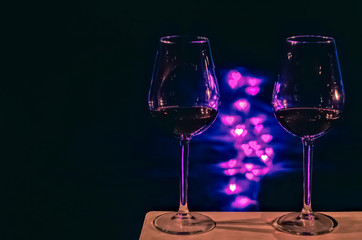 Two glasses of Red wine for a couple to celebrate Valentine's Day with love shape bokeh light on pink and blue light and black background.
