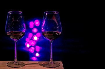 Two glasses of Red wine for a couple to celebrate Valentine's Day with round shape bokeh light on pink and blue light and black background.