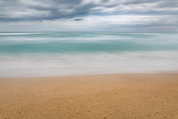Natural color layers of the cloudy sky, sea and sand, grey, turquoise, white and brown making a nice pattern at Tunquen Beach an awesome and wild beach with it wetlands and turquoise idyllic waters 