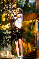 Obraz na płótnie Canvas Child in forest adventure park. Kid in white helmet and white t shirt climbs on high rope trail. Agility skills and climbing outdoor amusement center for children. young boy plays outdoors