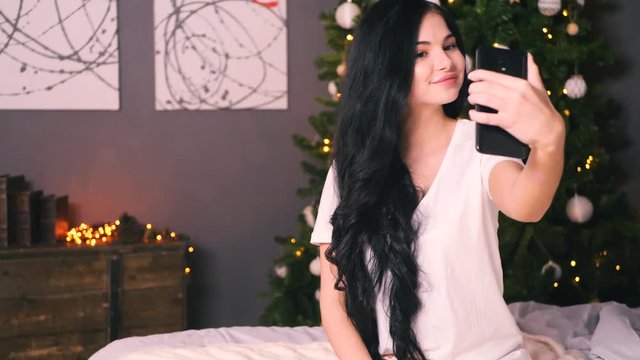 Young beautiful woman with decorated tree making selfy. New year's eve