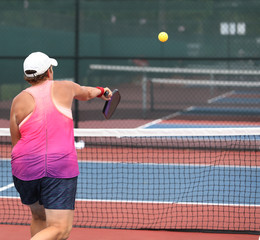 A senior lady returns a pickleball shot in a summer tournament. 
