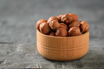 Wooden bowl with hazelnuts on a black wooden table.