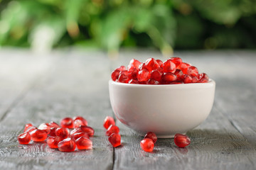 White bowl full of ripe pomegranate seeds on rustic table on green wood background. Harvest ripe pomegranate . Vegetarian food.