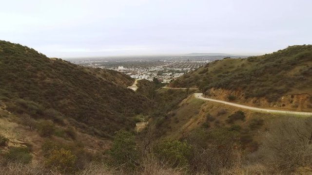 A wide overview establishing shot of Runyon Canyon in the hills of Los Angeles on an overcast day. Hikers on the trail in the distance.  	