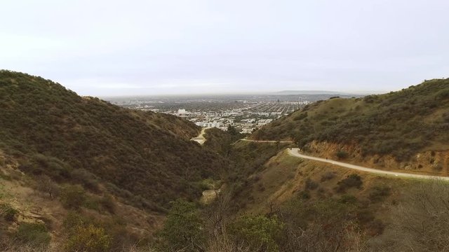 A wide overview establishing shot of Runyon Canyon in the hills of Los Angeles on an overcast day. Hikers on the trail in the distance.  	