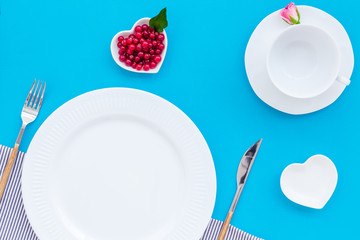 set-up table with plates, wineberry and flower on blue background top view mock-up