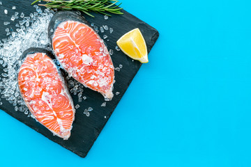 Raw salmon steak on black plate for cooking with lemon and rosemary on blue background top view mockup