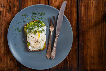 Toast with avocado and poached egg on round gray plate blackboard. Copy space Top view.