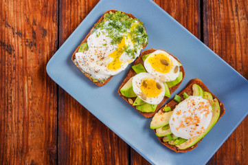 Toasts with avocado and fried egg on a rectangular gray plate. Top view