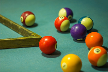 multicolored blurred billiard balls with numbers are on the table with blue cloth and wooden pyromid