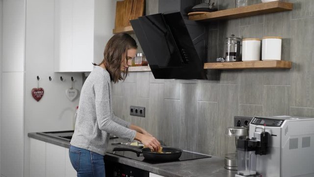 Beautiful brunnete girl cooking dinner in home kitchen, frying on a pan.